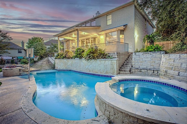 pool at dusk featuring stairway, a pool with connected hot tub, and fence