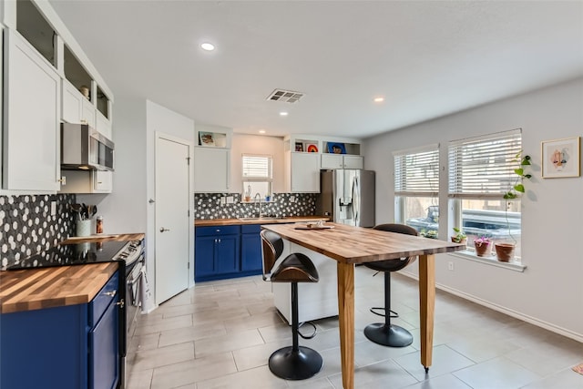 kitchen with white cabinets, blue cabinets, stainless steel appliances, and wooden counters