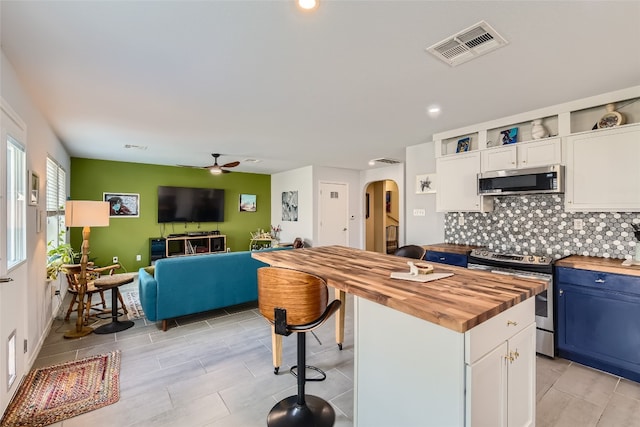 kitchen featuring wooden counters, decorative backsplash, blue cabinetry, appliances with stainless steel finishes, and white cabinetry