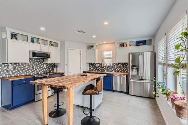 kitchen featuring butcher block counters, tasteful backsplash, blue cabinets, white cabinets, and appliances with stainless steel finishes