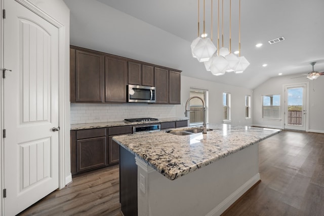 kitchen with light stone countertops, sink, hanging light fixtures, stainless steel appliances, and a kitchen island with sink