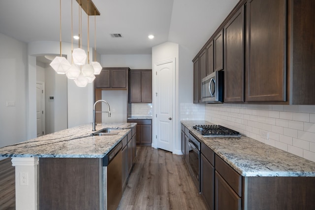 kitchen with light stone countertops, hardwood / wood-style flooring, stainless steel appliances, sink, and decorative light fixtures