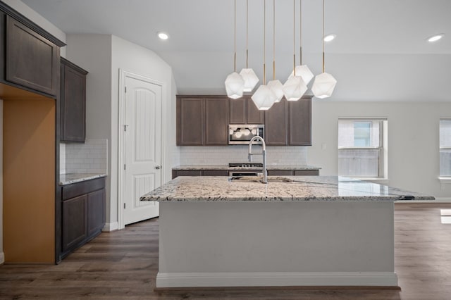 kitchen with a center island with sink, dark wood-type flooring, and light stone countertops