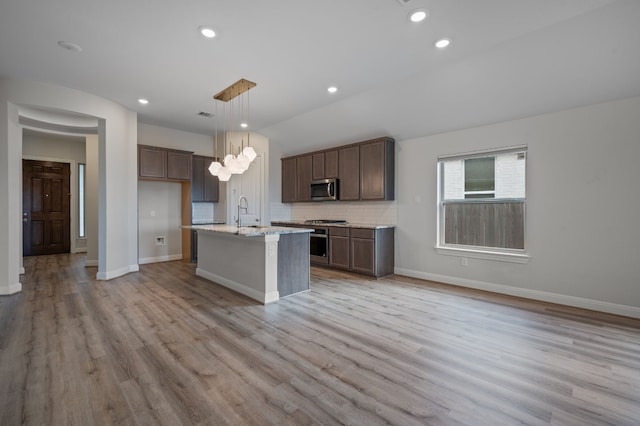 kitchen featuring light hardwood / wood-style floors, stainless steel appliances, a kitchen island with sink, and hanging light fixtures