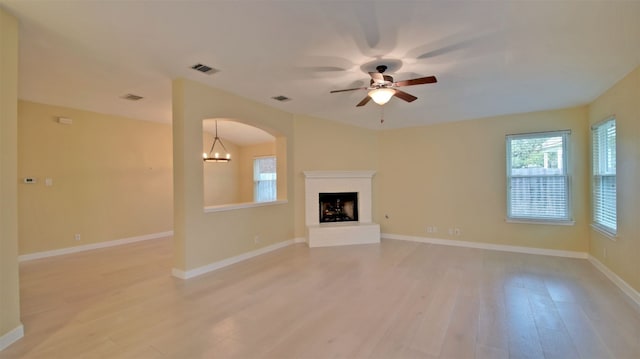 unfurnished living room with ceiling fan with notable chandelier and light hardwood / wood-style flooring