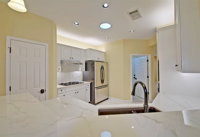 kitchen with light stone countertops, sink, tasteful backsplash, stainless steel fridge, and white cabinets