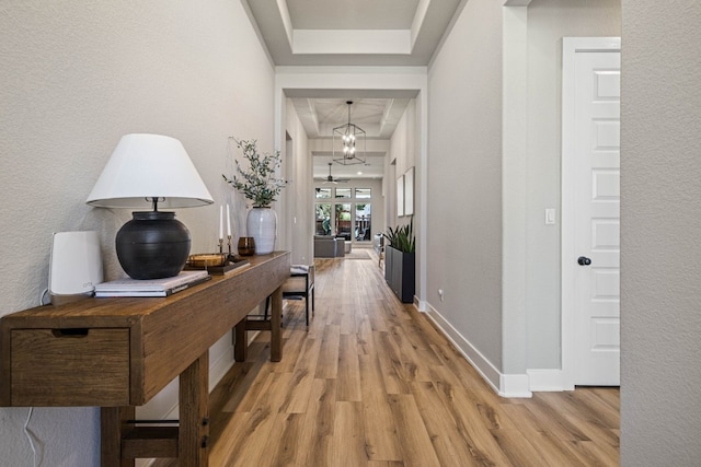 hallway with a tray ceiling and light wood-type flooring