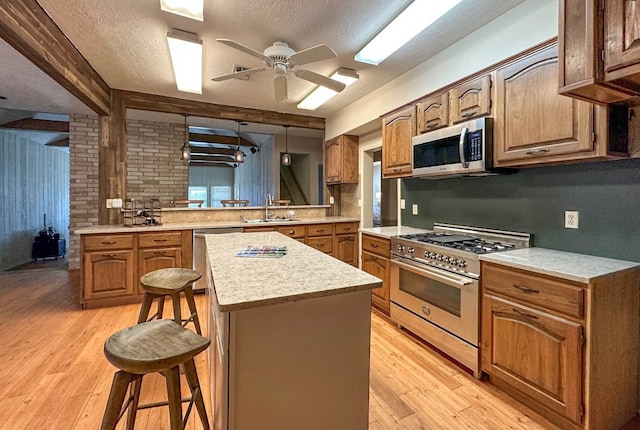 kitchen with appliances with stainless steel finishes, sink, kitchen peninsula, a kitchen breakfast bar, and light hardwood / wood-style flooring