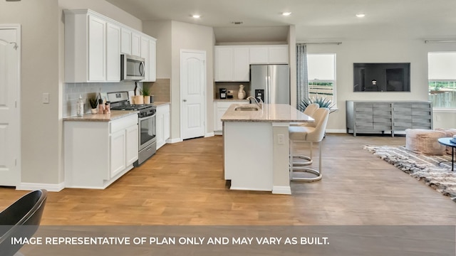 kitchen featuring a center island with sink, white cabinetry, light wood-type flooring, stainless steel appliances, and sink