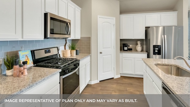 kitchen with appliances with stainless steel finishes, white cabinets, sink, and light hardwood / wood-style floors