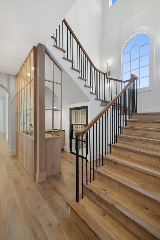 stairway with wood-type flooring and a towering ceiling