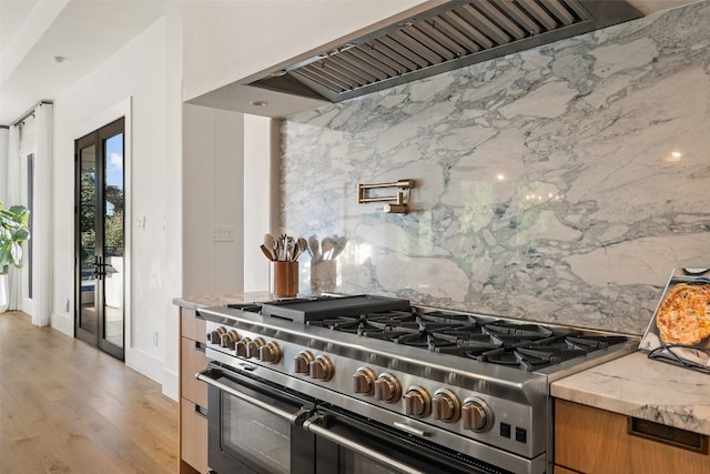 kitchen featuring light stone countertops, light hardwood / wood-style floors, high end stainless steel range oven, and extractor fan