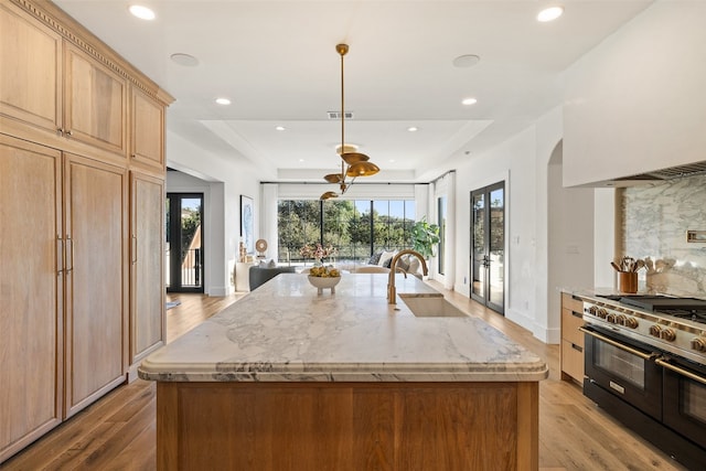 kitchen with sink, an island with sink, range with two ovens, and light hardwood / wood-style floors