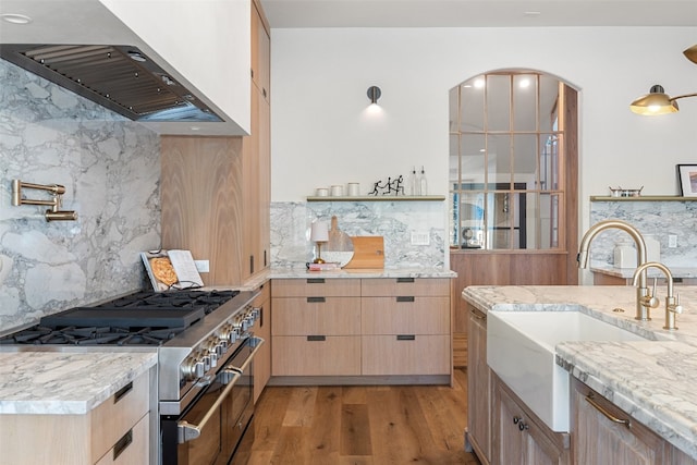 kitchen with high end stove, light brown cabinets, exhaust hood, light hardwood / wood-style flooring, and backsplash