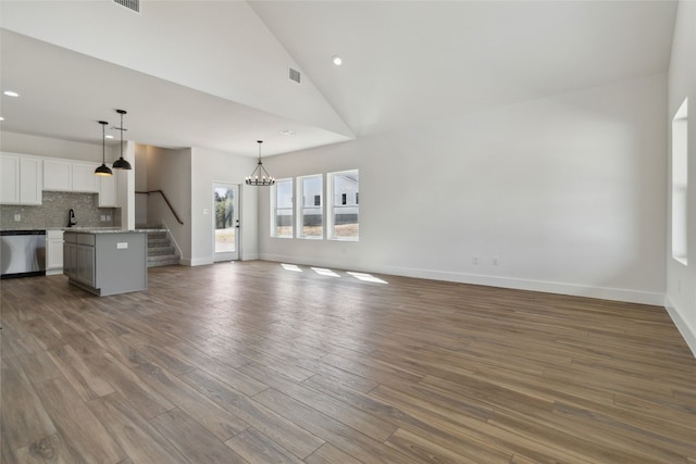 unfurnished living room with sink, a chandelier, high vaulted ceiling, and light wood-type flooring