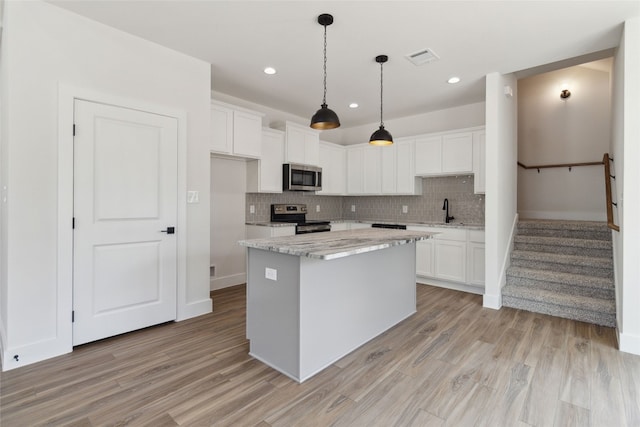 kitchen with appliances with stainless steel finishes, light wood-type flooring, backsplash, a center island, and white cabinets