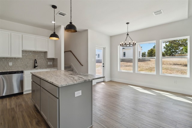 kitchen featuring white cabinetry, light hardwood / wood-style floors, decorative light fixtures, stainless steel dishwasher, and light stone counters