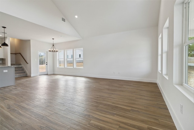 unfurnished living room with a notable chandelier, dark hardwood / wood-style floors, high vaulted ceiling, and plenty of natural light