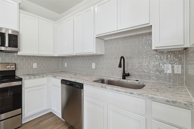 kitchen with appliances with stainless steel finishes, white cabinets, sink, and light hardwood / wood-style floors