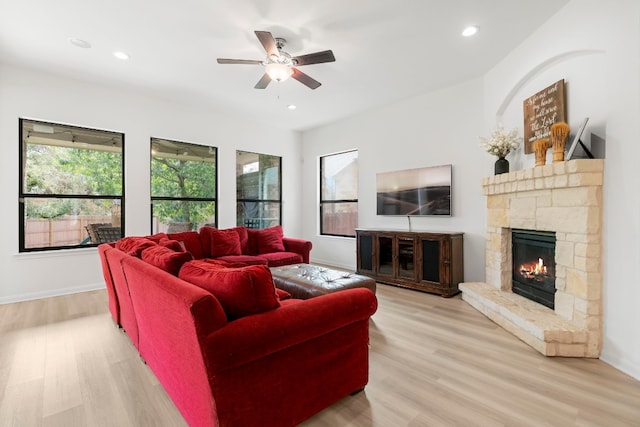 living room with a stone fireplace, ceiling fan, and light hardwood / wood-style flooring