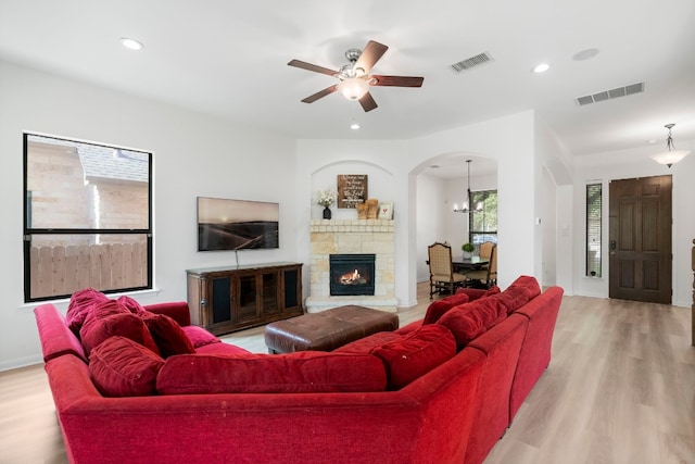 living room with a fireplace, light hardwood / wood-style floors, and ceiling fan with notable chandelier