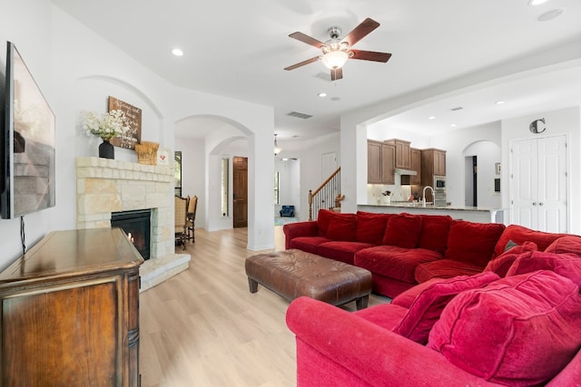 living room with ceiling fan, light wood-type flooring, and a stone fireplace