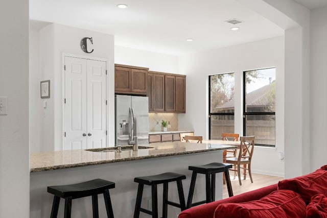 kitchen with light stone countertops, stainless steel refrigerator with ice dispenser, decorative backsplash, a breakfast bar, and light hardwood / wood-style flooring