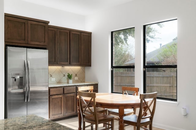 kitchen with light stone countertops, stainless steel fridge, backsplash, and dark brown cabinets