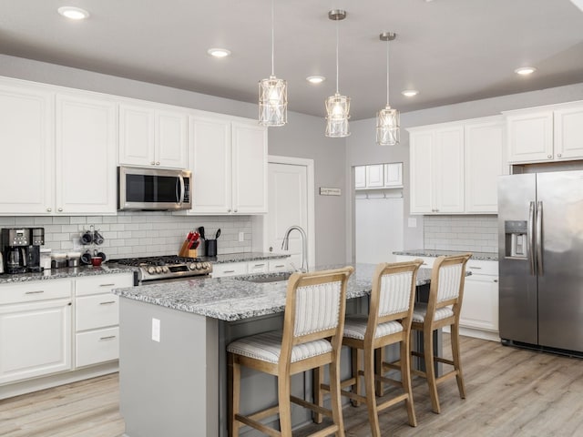 kitchen featuring appliances with stainless steel finishes, a kitchen island with sink, white cabinetry, and tasteful backsplash