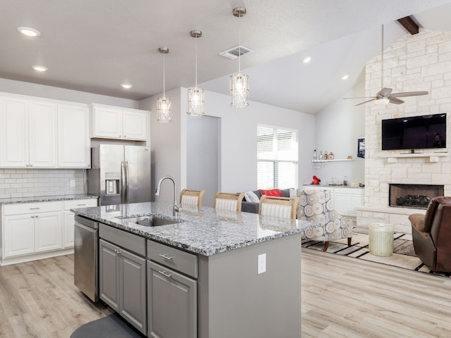 kitchen featuring white cabinets, an island with sink, stainless steel appliances, lofted ceiling with beams, and sink