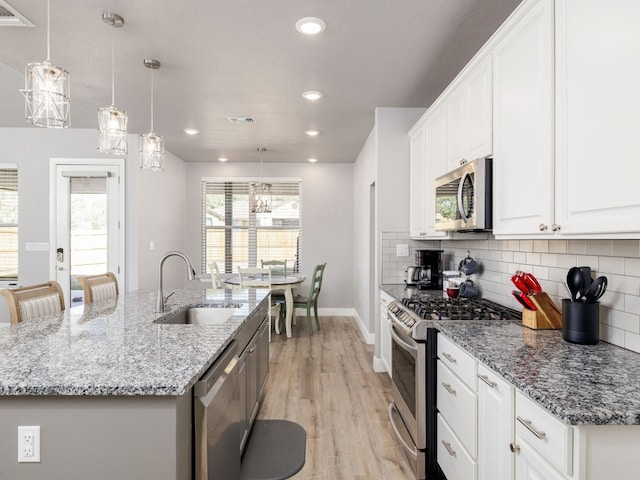 kitchen with sink, appliances with stainless steel finishes, white cabinetry, and an island with sink