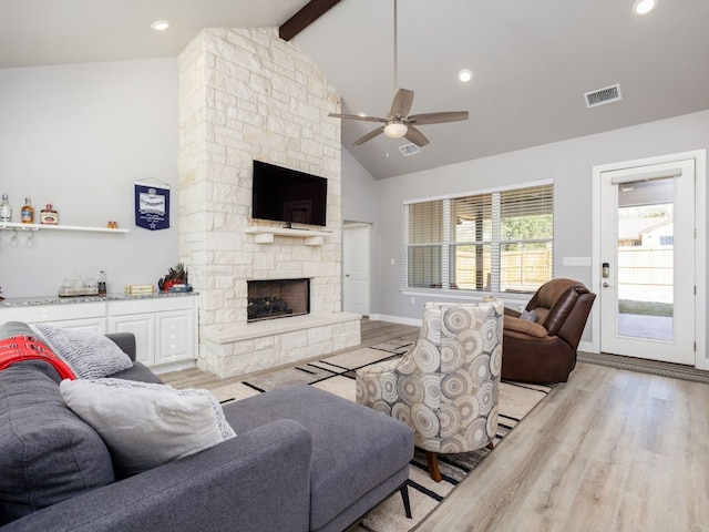 living room featuring ceiling fan, high vaulted ceiling, beamed ceiling, a fireplace, and light hardwood / wood-style floors