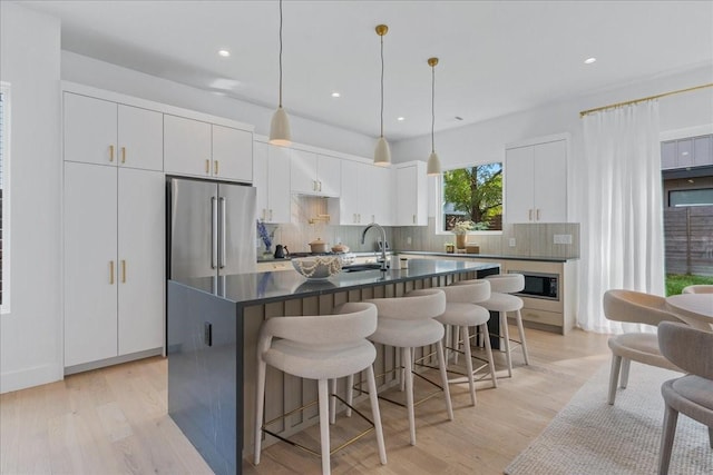 kitchen featuring built in microwave, high quality fridge, an island with sink, white cabinets, and backsplash