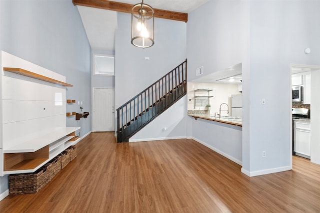 interior space featuring sink, beam ceiling, a towering ceiling, and light hardwood / wood-style flooring