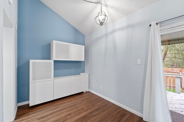 unfurnished bedroom with a notable chandelier, a textured ceiling, dark wood-type flooring, and vaulted ceiling