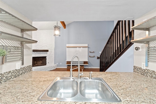 kitchen with sink, a fireplace, pendant lighting, beam ceiling, and hardwood / wood-style flooring