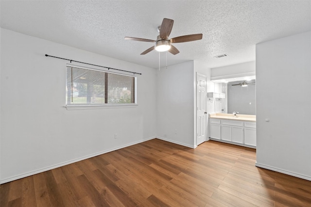 unfurnished bedroom with light hardwood / wood-style flooring, a textured ceiling, ensuite bath, and ceiling fan