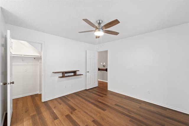 unfurnished bedroom with a spacious closet, a textured ceiling, dark hardwood / wood-style flooring, a closet, and ceiling fan