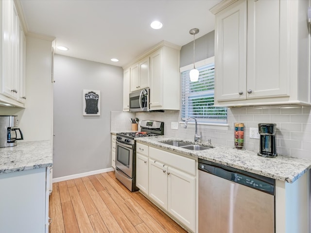 kitchen featuring hanging light fixtures, backsplash, appliances with stainless steel finishes, light wood-type flooring, and sink