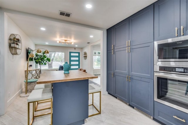 kitchen with blue cabinetry, wooden counters, appliances with stainless steel finishes, a kitchen bar, and a kitchen island