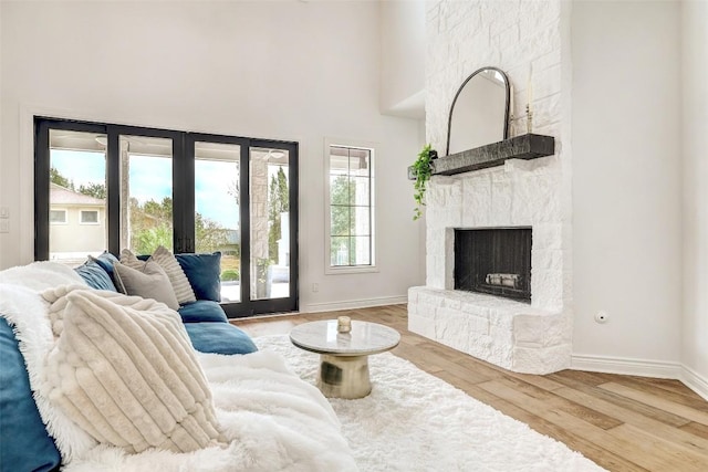 living room featuring hardwood / wood-style flooring, a stone fireplace, a towering ceiling, and french doors