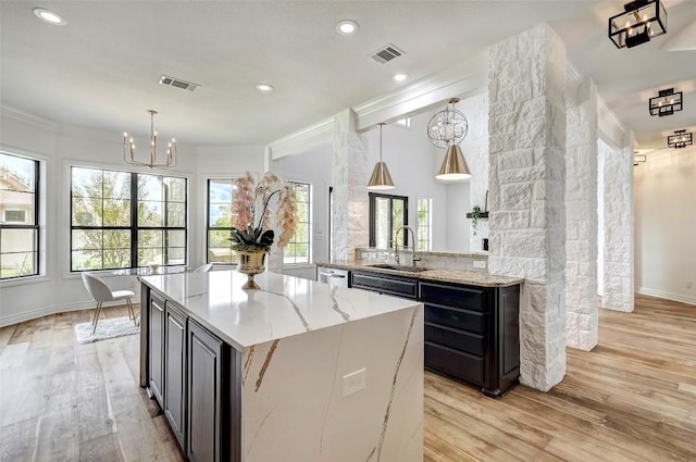 kitchen with light stone counters, decorative light fixtures, sink, and light wood-type flooring