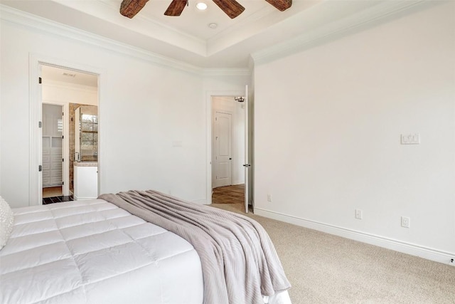 carpeted bedroom with connected bathroom, a tray ceiling, ornamental molding, and ceiling fan