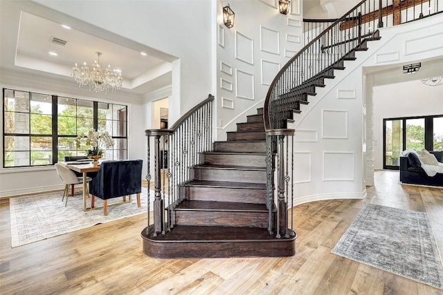 stairway with hardwood / wood-style floors, a tray ceiling, a notable chandelier, and a high ceiling