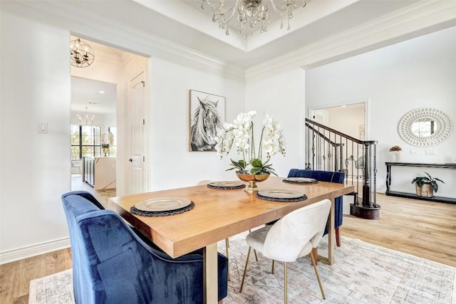 dining room with an inviting chandelier, crown molding, a raised ceiling, and light wood-type flooring