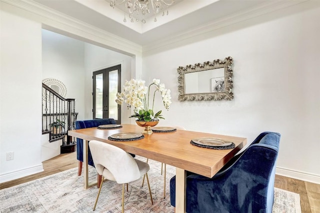 dining space with hardwood / wood-style floors, ornamental molding, a tray ceiling, an inviting chandelier, and french doors