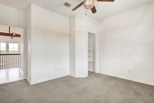 unfurnished bedroom featuring beamed ceiling, ceiling fan, carpet, and a walk in closet