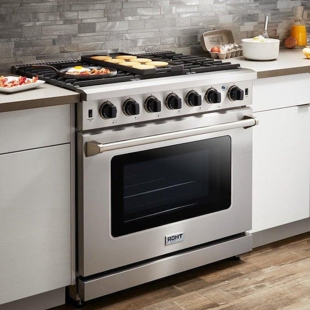 details featuring decorative backsplash, white cabinetry, stainless steel stove, and light hardwood / wood-style flooring