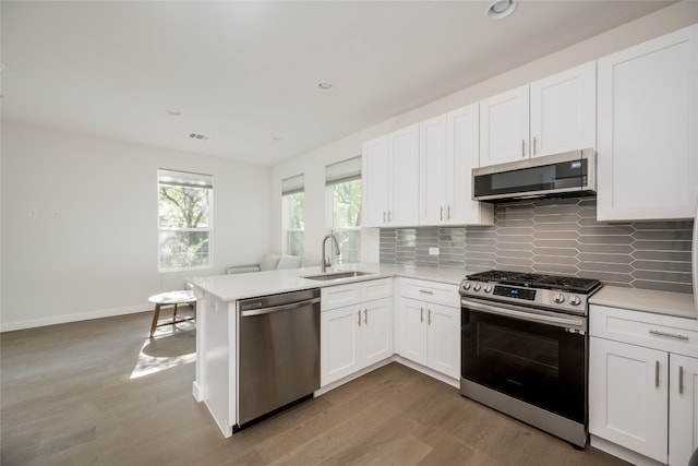 kitchen with appliances with stainless steel finishes, kitchen peninsula, white cabinets, and sink