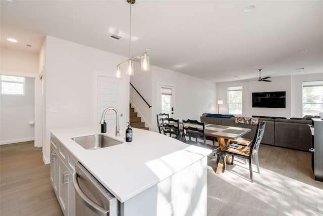 kitchen featuring sink, an island with sink, dishwasher, decorative light fixtures, and light hardwood / wood-style flooring